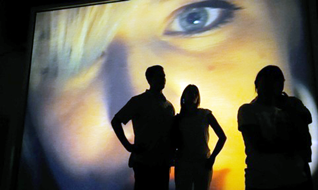 three people looking at a large projection of a person's face