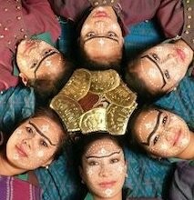 six performers lying down, their faces in a circular pattern.
