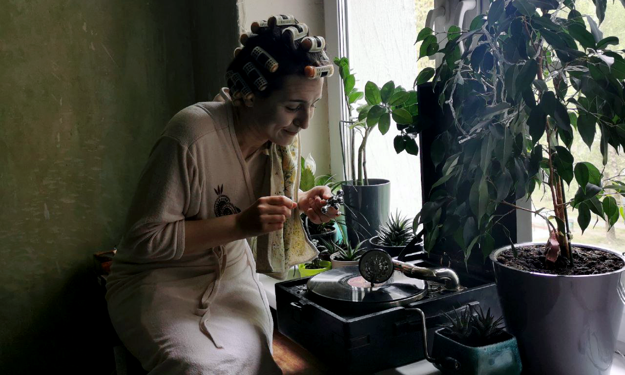 a person in curlers and a robe seated in front of a record player and plants