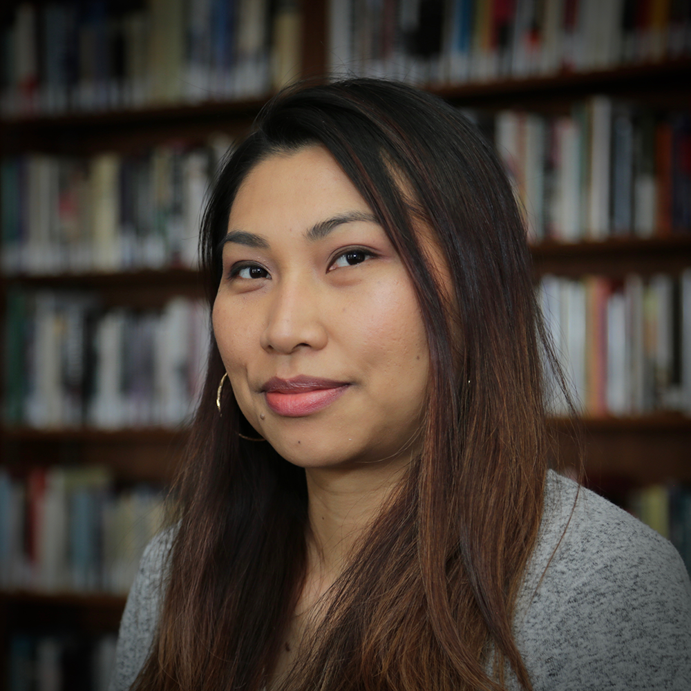 Portrait of Saymoukda Duangphouxay Vongsay smiling in front of a bookshelf.