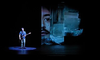 an actor onstage with a large projection behind them