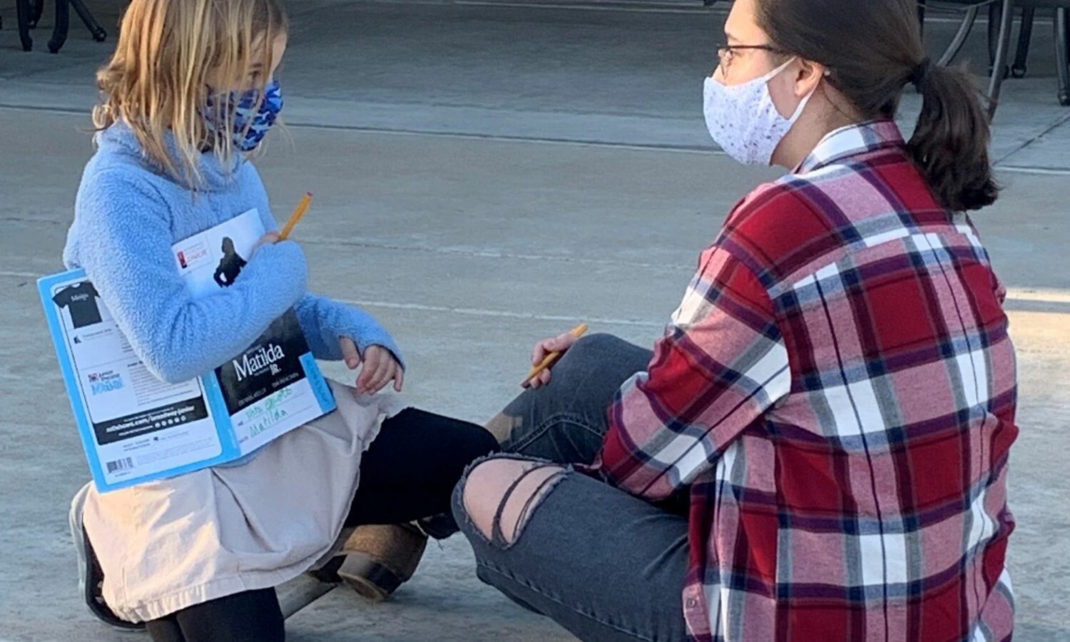 An instructor siting on the ground with a young actor who's holding a script titled Matilda Jr.