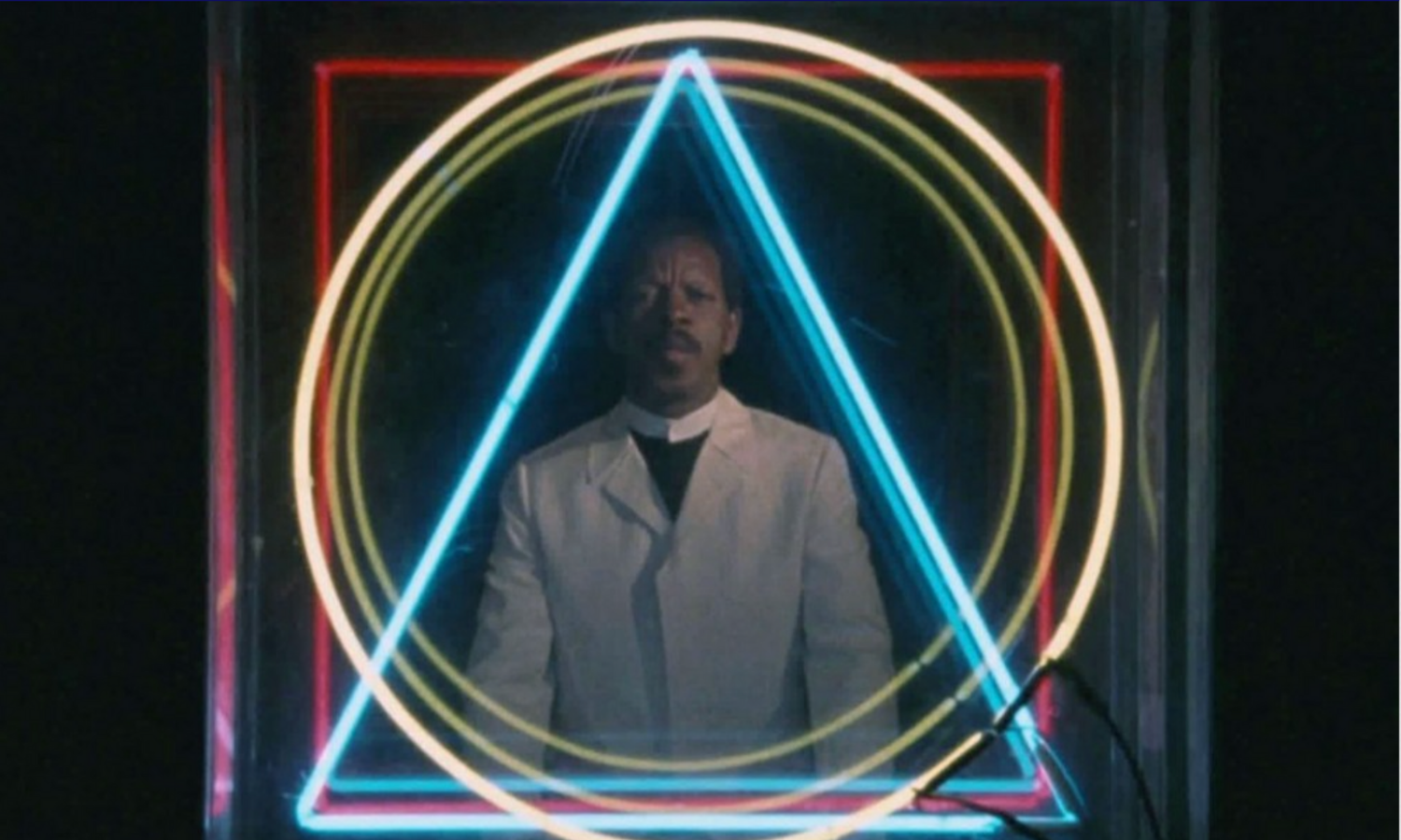 Ornette Coleman standing behind overlapping neon circles and a neon triangle.