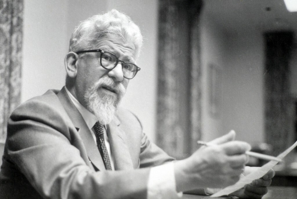 Rabbi Abraham Joshua Heschel sitting down and holding a pencil and paper.