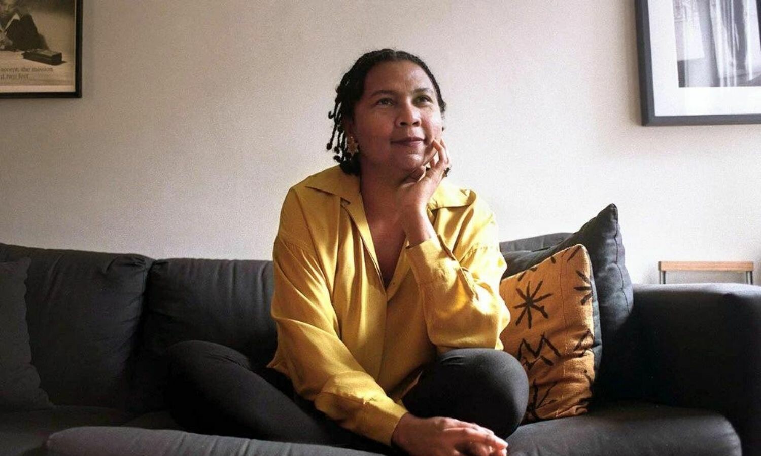 bell hooks sitting on a dark gray couch with a slight smile.