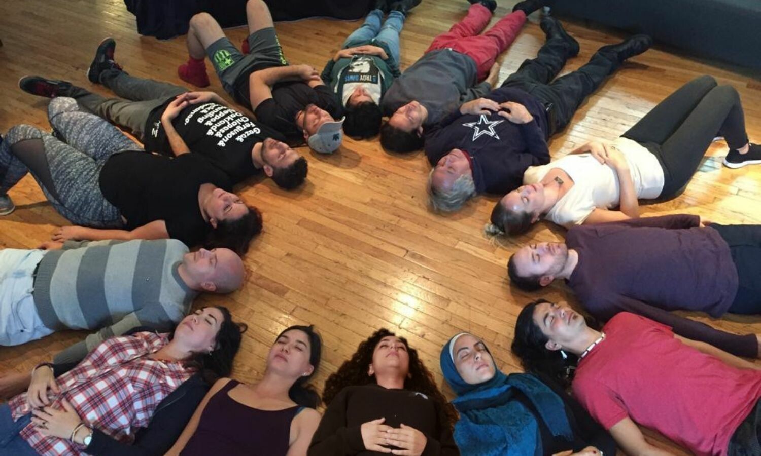 Fourteen people laid down with their backs against the ground in a circle.