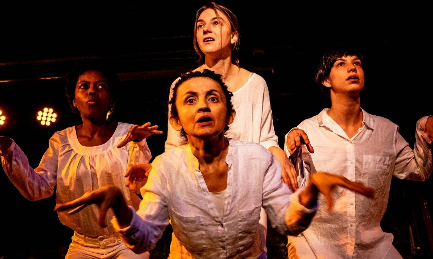 Four actresses, dressed in white, making delirious facial expressions and flopping their wrists downward with their fingers hanging freely.