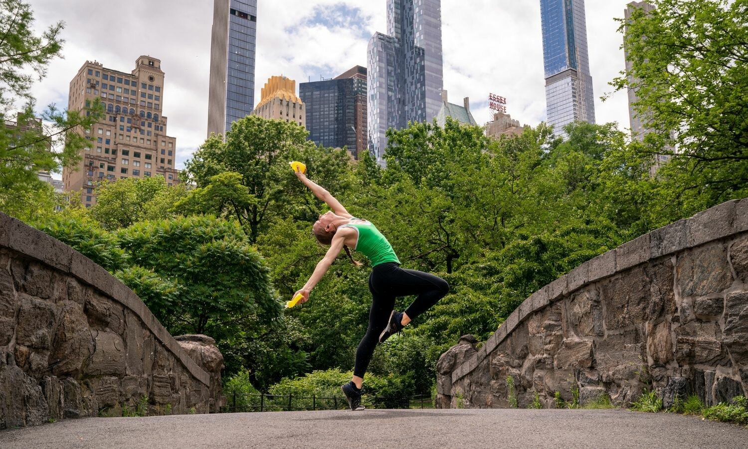 A woman in athletic clothing dances on a bridge in Central Park, New York City.
