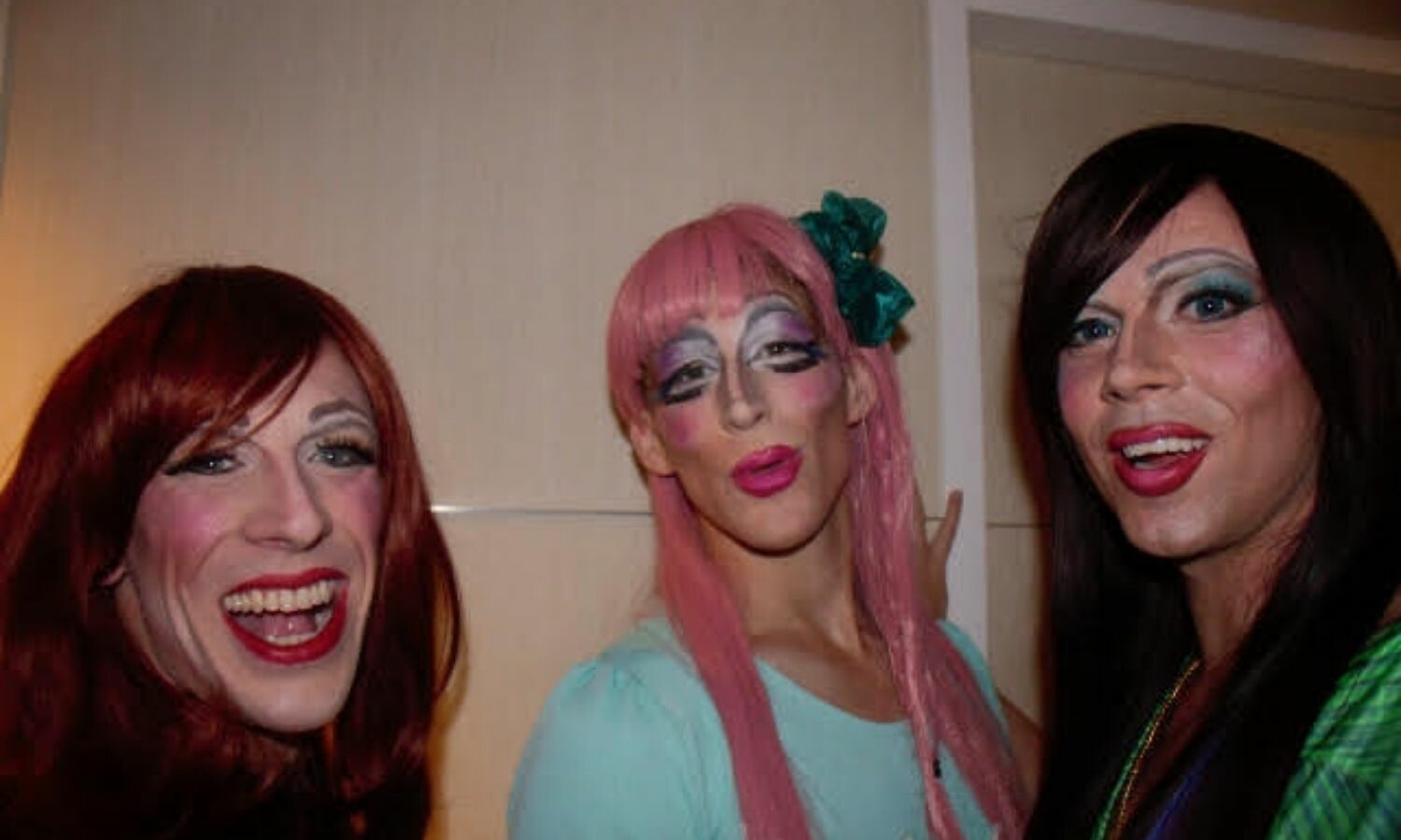 Three men wearing a drag queen look using wigs and makeup.