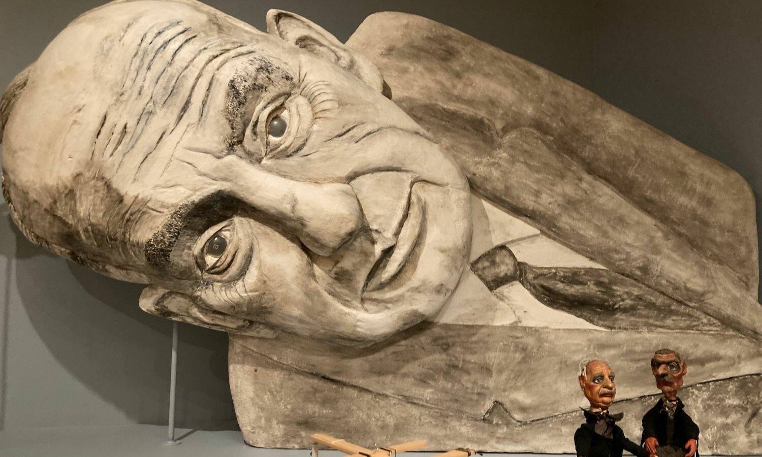 A large, titled puppet depiction of the American designer Robert Moses with two tiny brown-skinned puppets in front.
