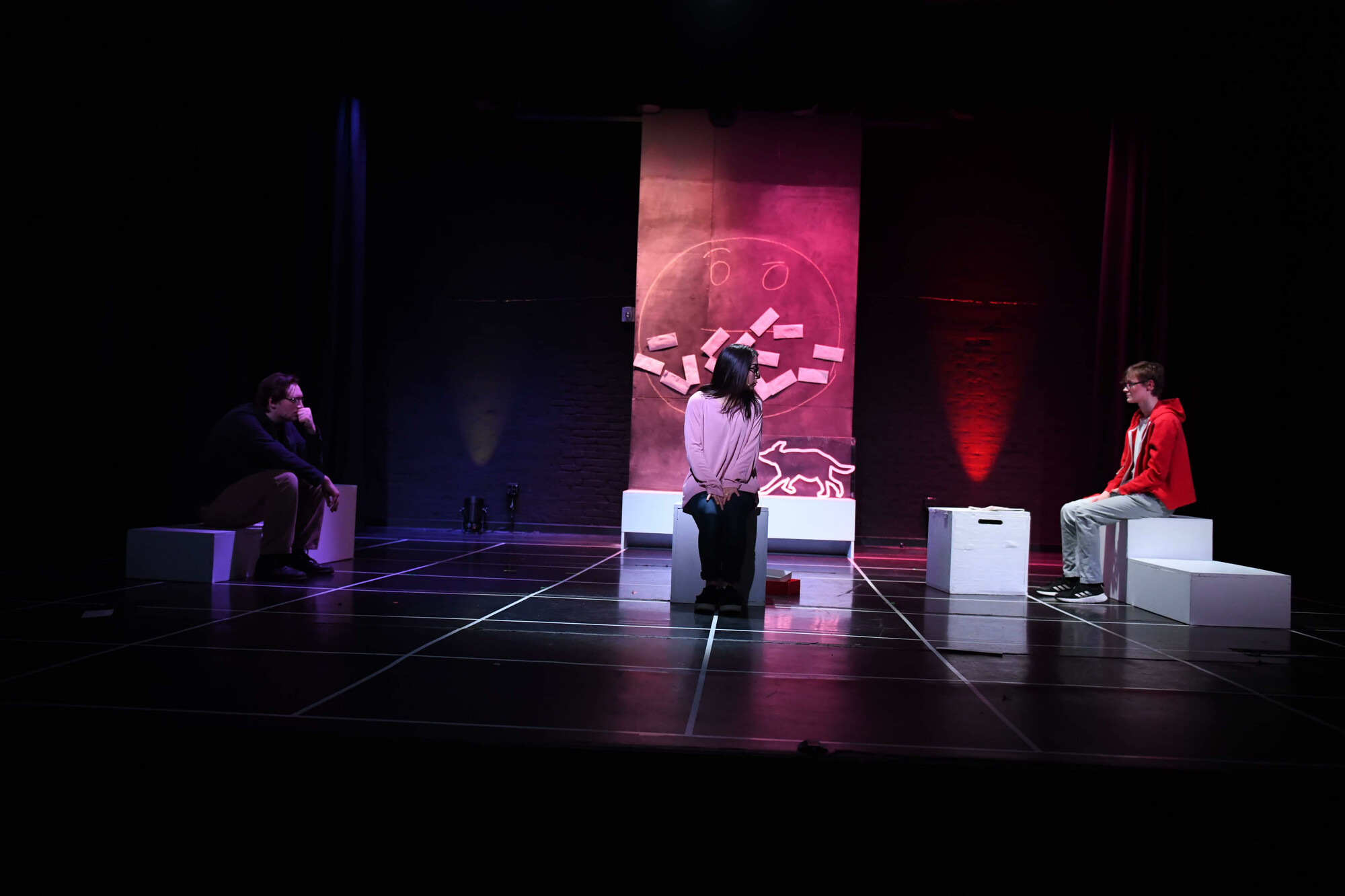 Three actors sitting on white cubes onstage.