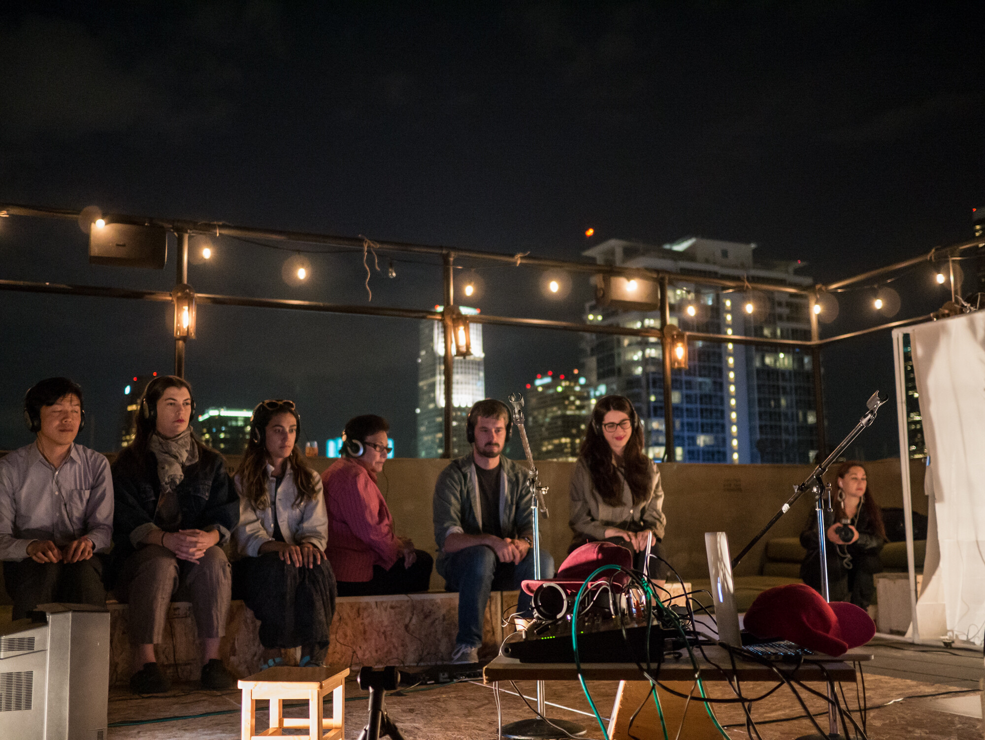 Seven people sitting on a lit-up rooftop.