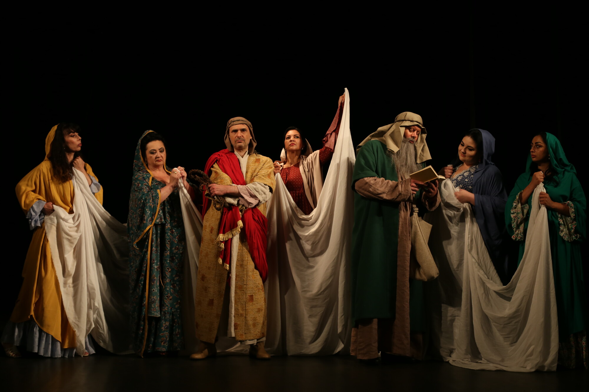 Seven people wearing ancient clothing and holding white cloth.