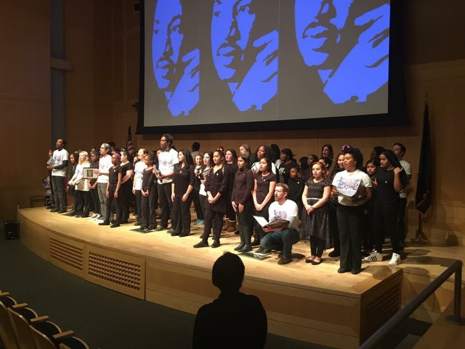 People performing on a stage with image of Martin Luther Kings projected behind them in blue.