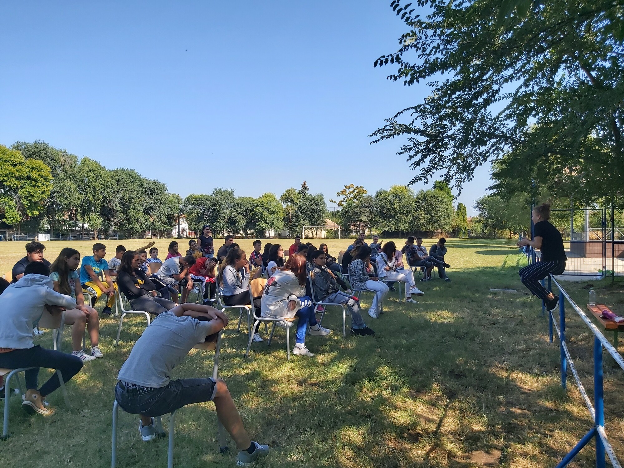 Image of people sitting outdoors at a park during a performance.