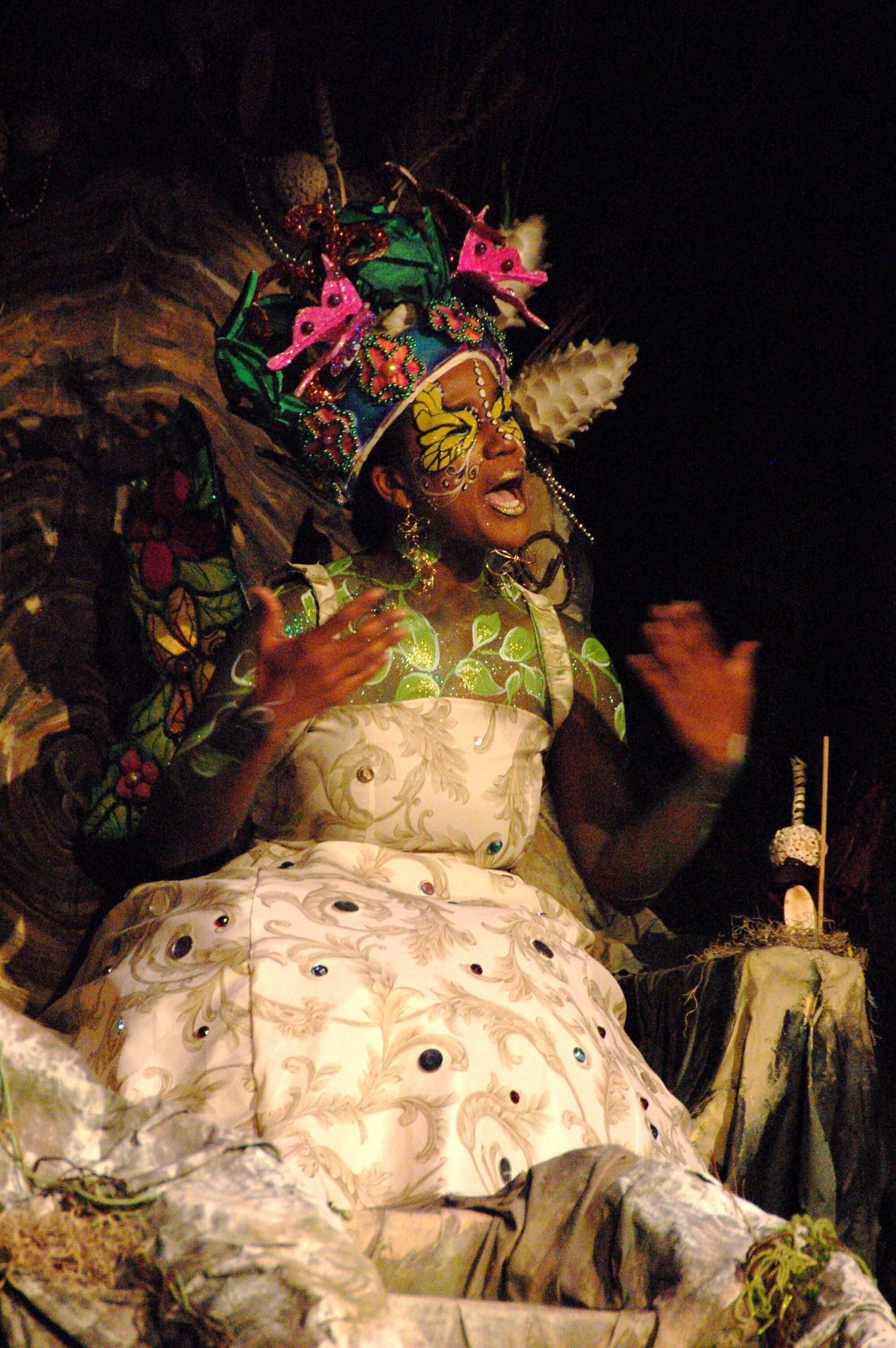 A Black actress in a dress and wearing a decorative headdress performing on stage.