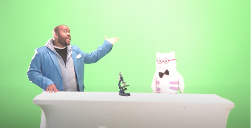 A man talks to a puppet in front of a green screen.