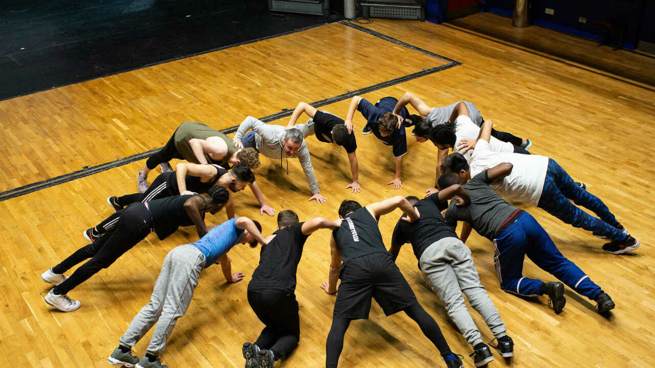 Several actors in a circle on the floor.