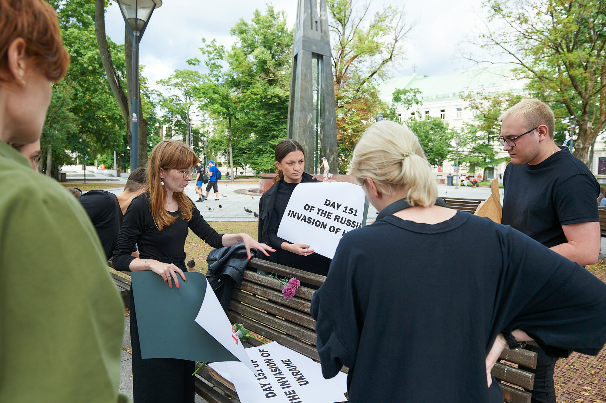 Several people in black shirts organize signs on a park bench.
