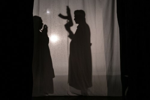 silhouette of actor behind a curtain holding a gun.