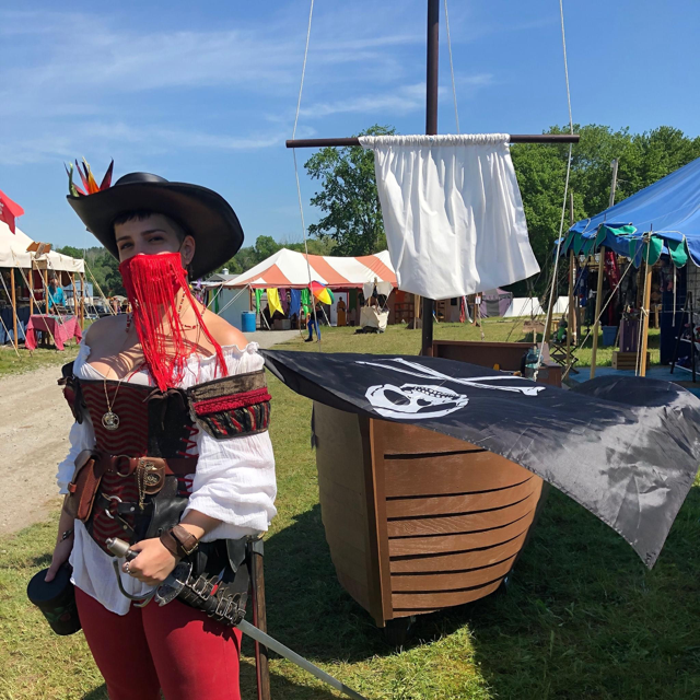 A performer dressed as a pirate with a model pirate ship behind them.