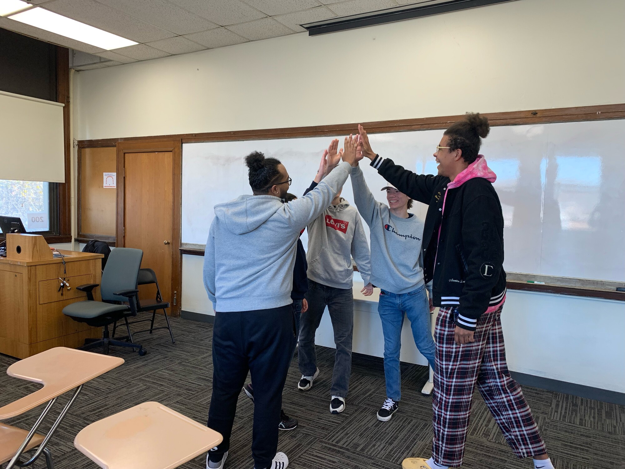 Five people gather in a circle and high five in the center in a classroom.