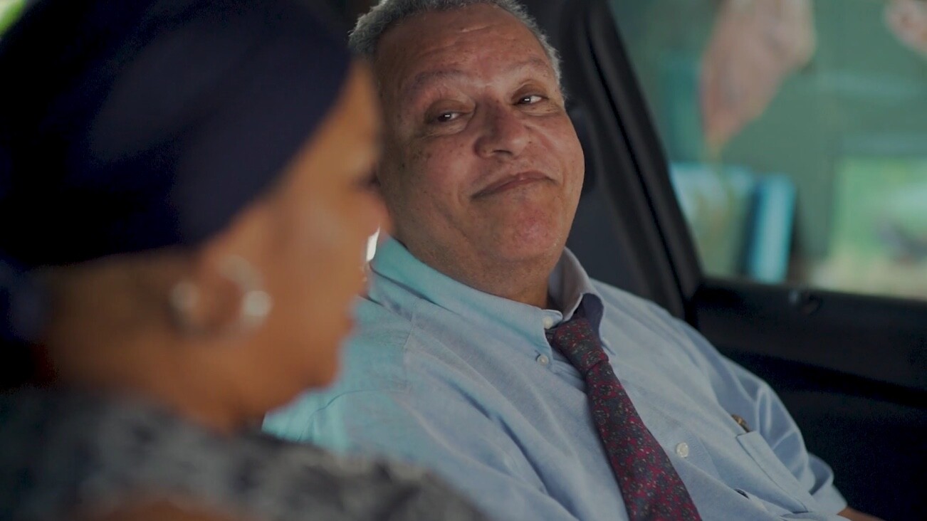 A man seated in a car smiles at a woman next to him in the passenger seat.