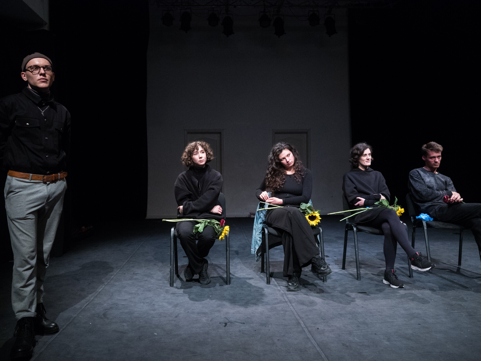 One performer stands next to four seated performers who hold sunflowers in their laps.