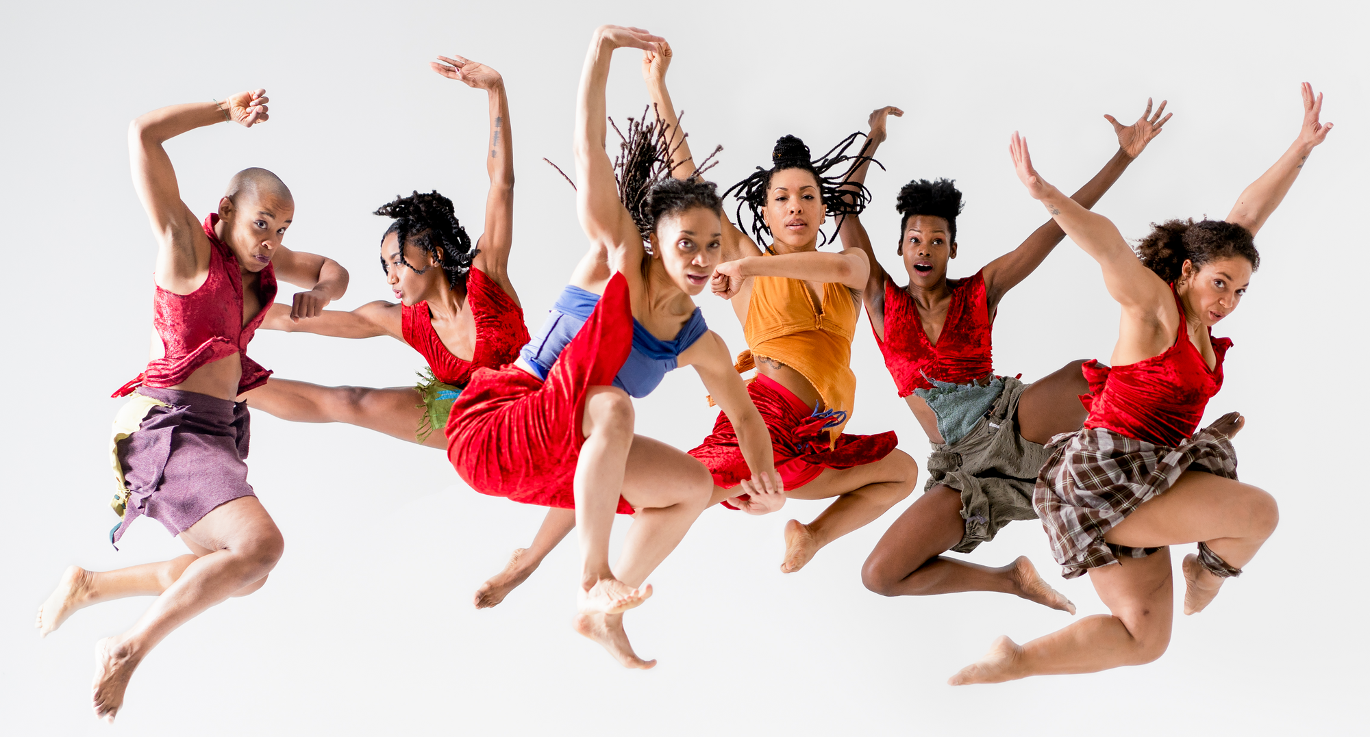 Six dancers dressed in red jumping in the air together.