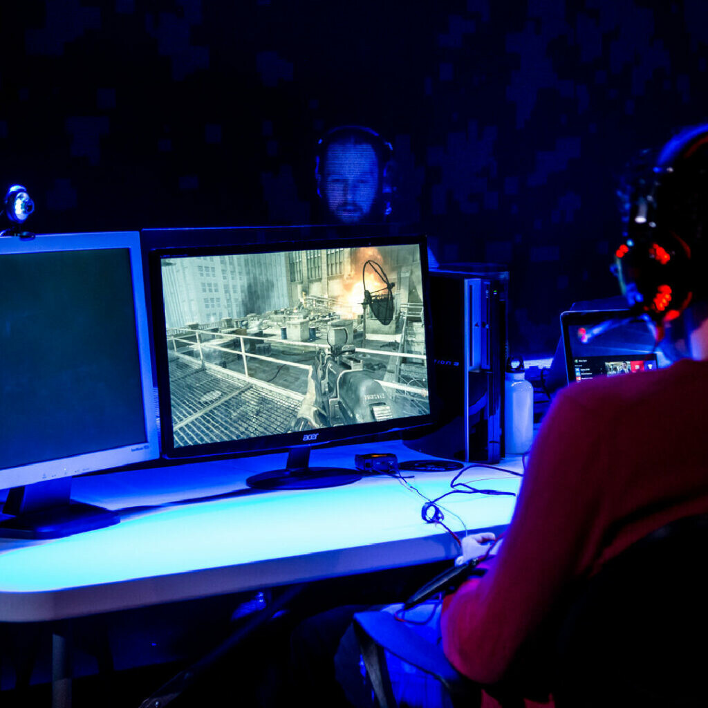 Two performers at gaming desks playing Call of Duty on-stage.