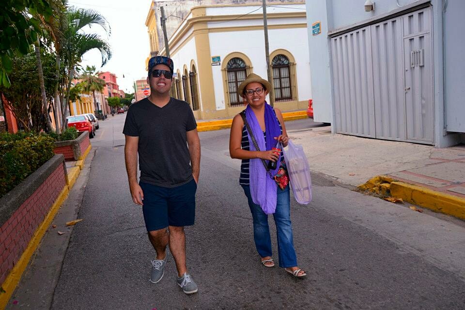 Two people smile at the camera while walking down a street.
