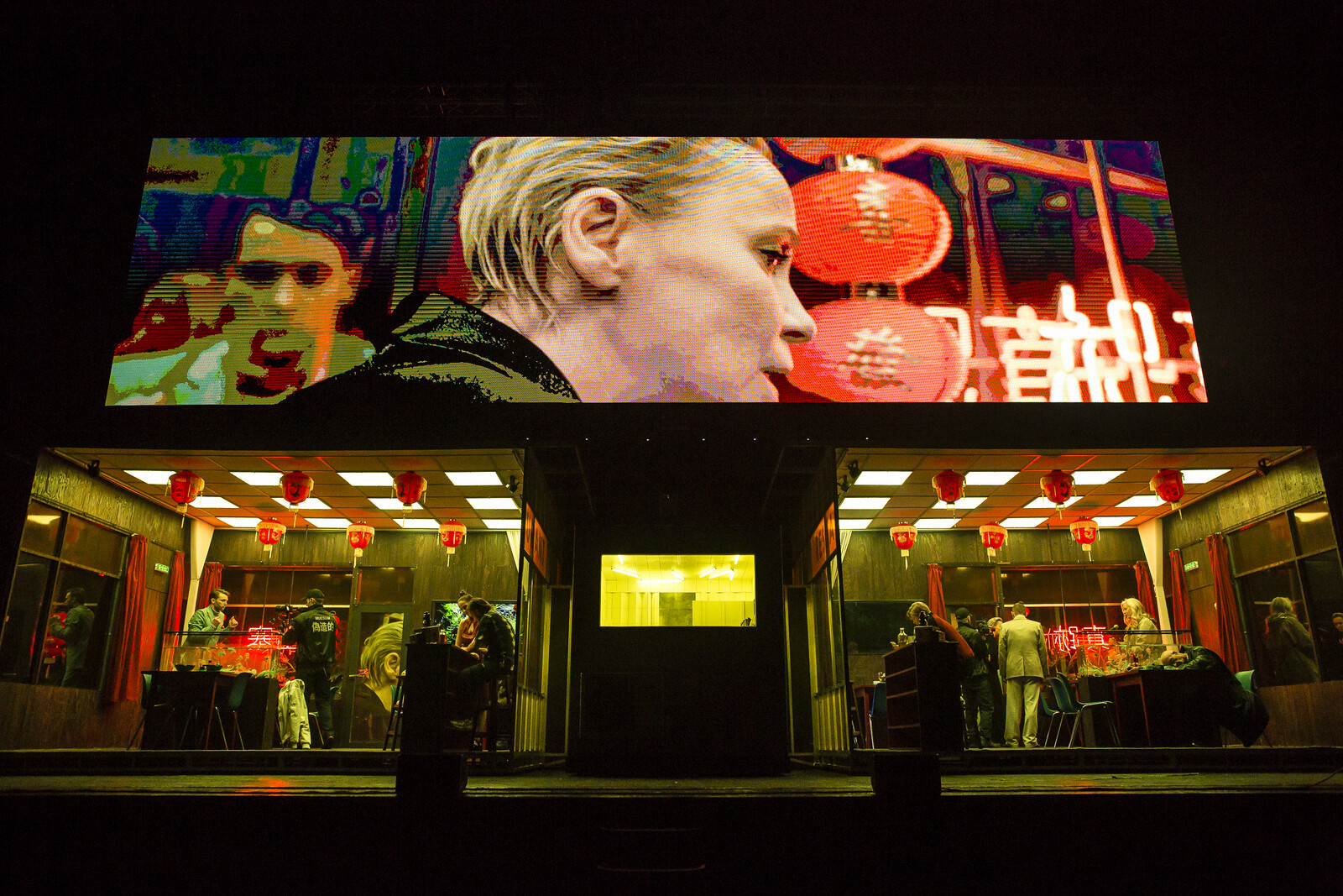 Actors move about two separate Chinese restaurant sets while a video plays above them on a massive screen that spans the width of the stage.