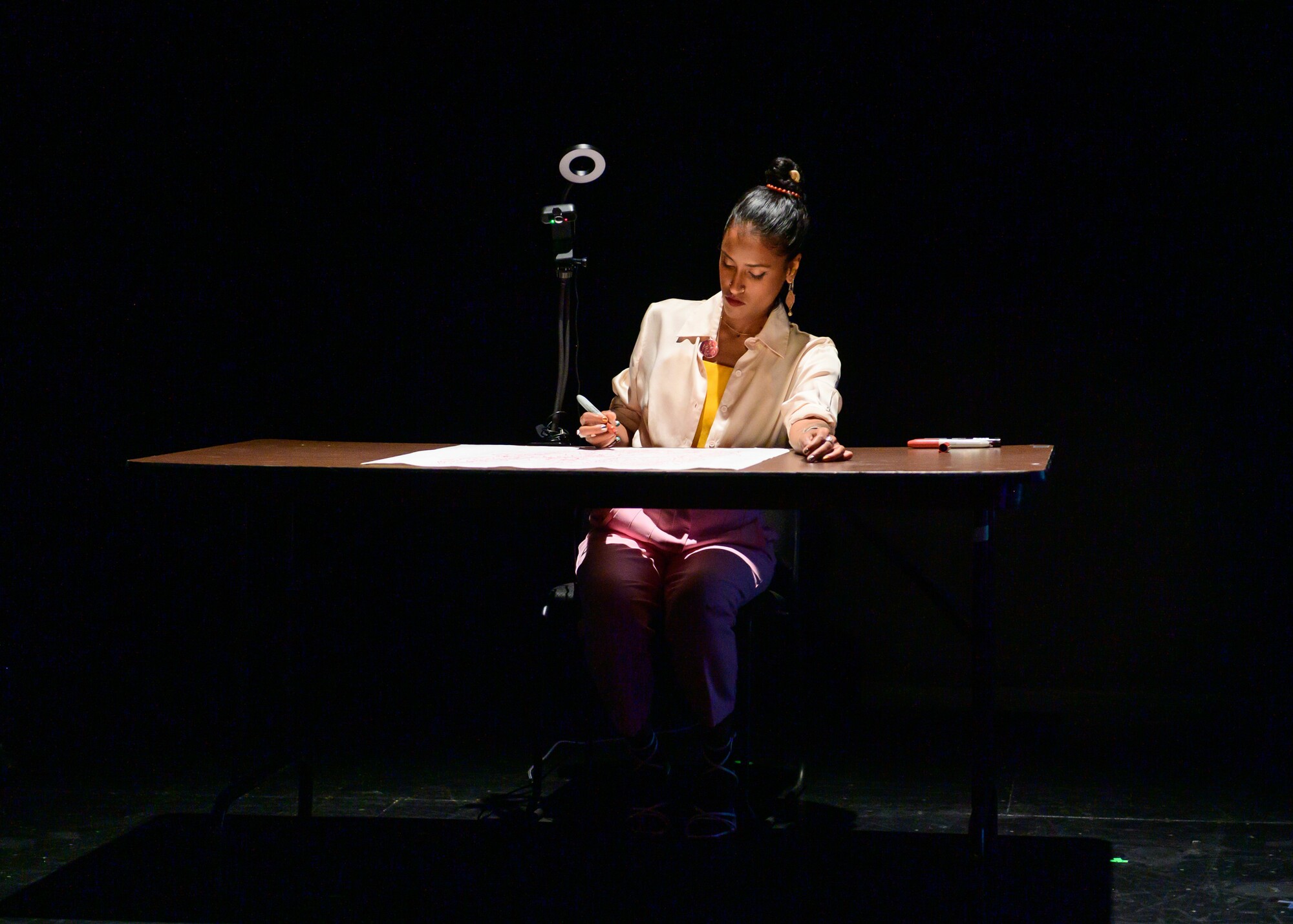 A woman sits at a desk and writes on-stage.