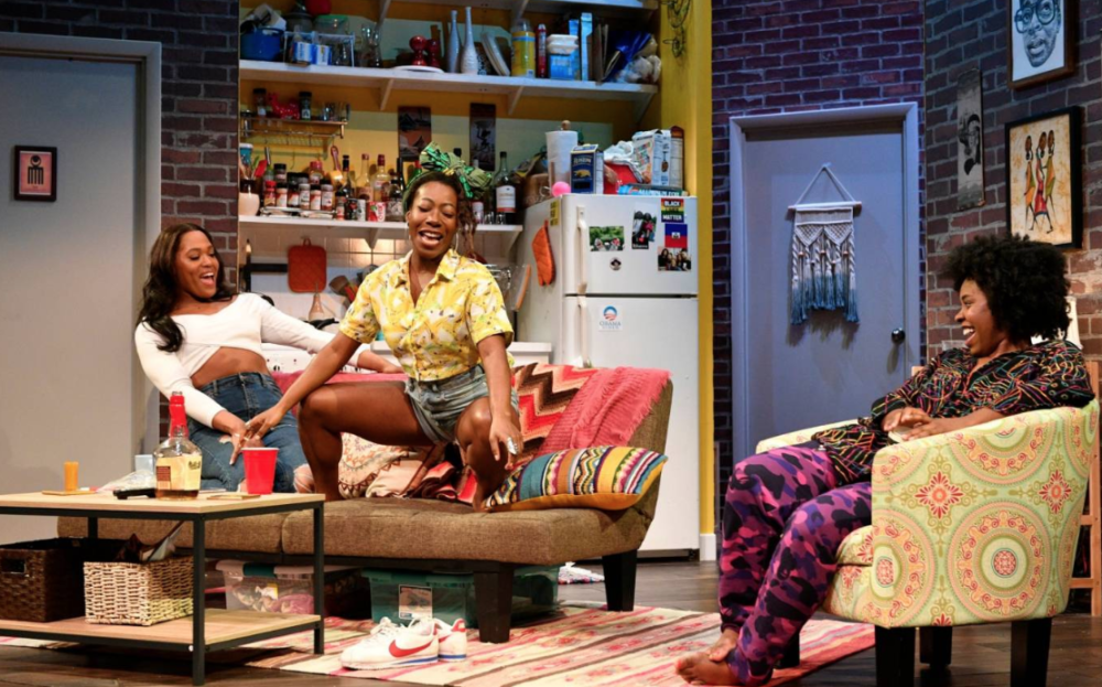 Three performers sit on couches and chairs on a brightly colored living room set.