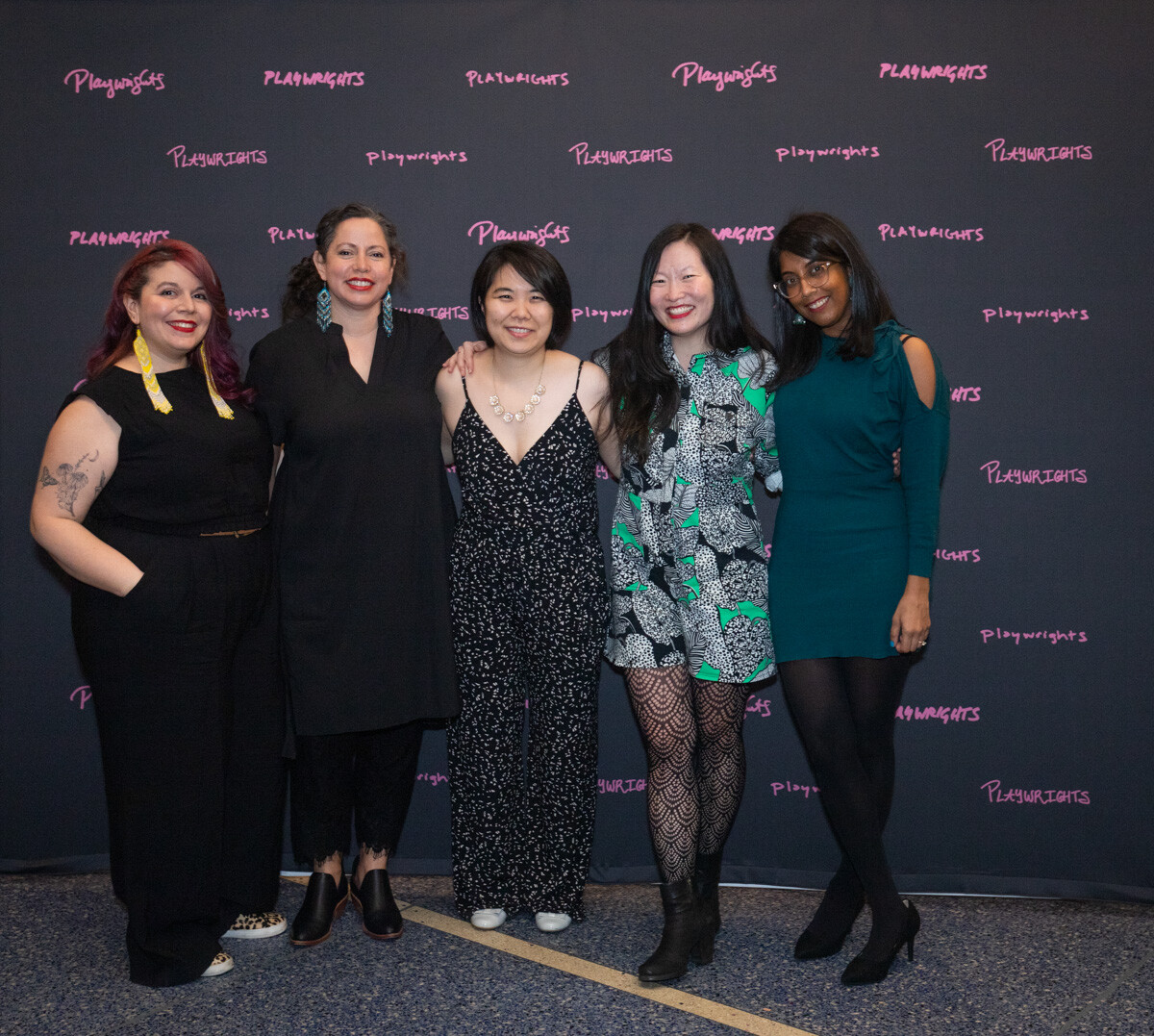 Five women pose in front of a premiere backdrop and smile.