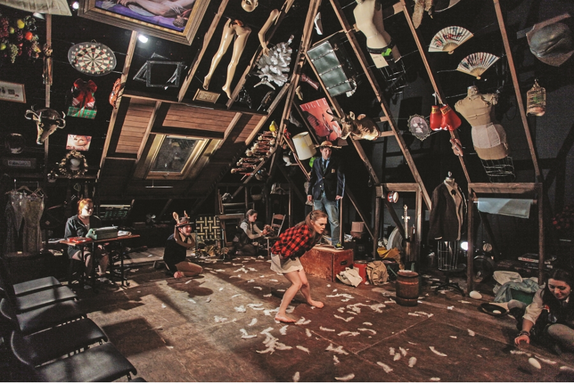 Five people performing in a large room with black walls covered in random items.