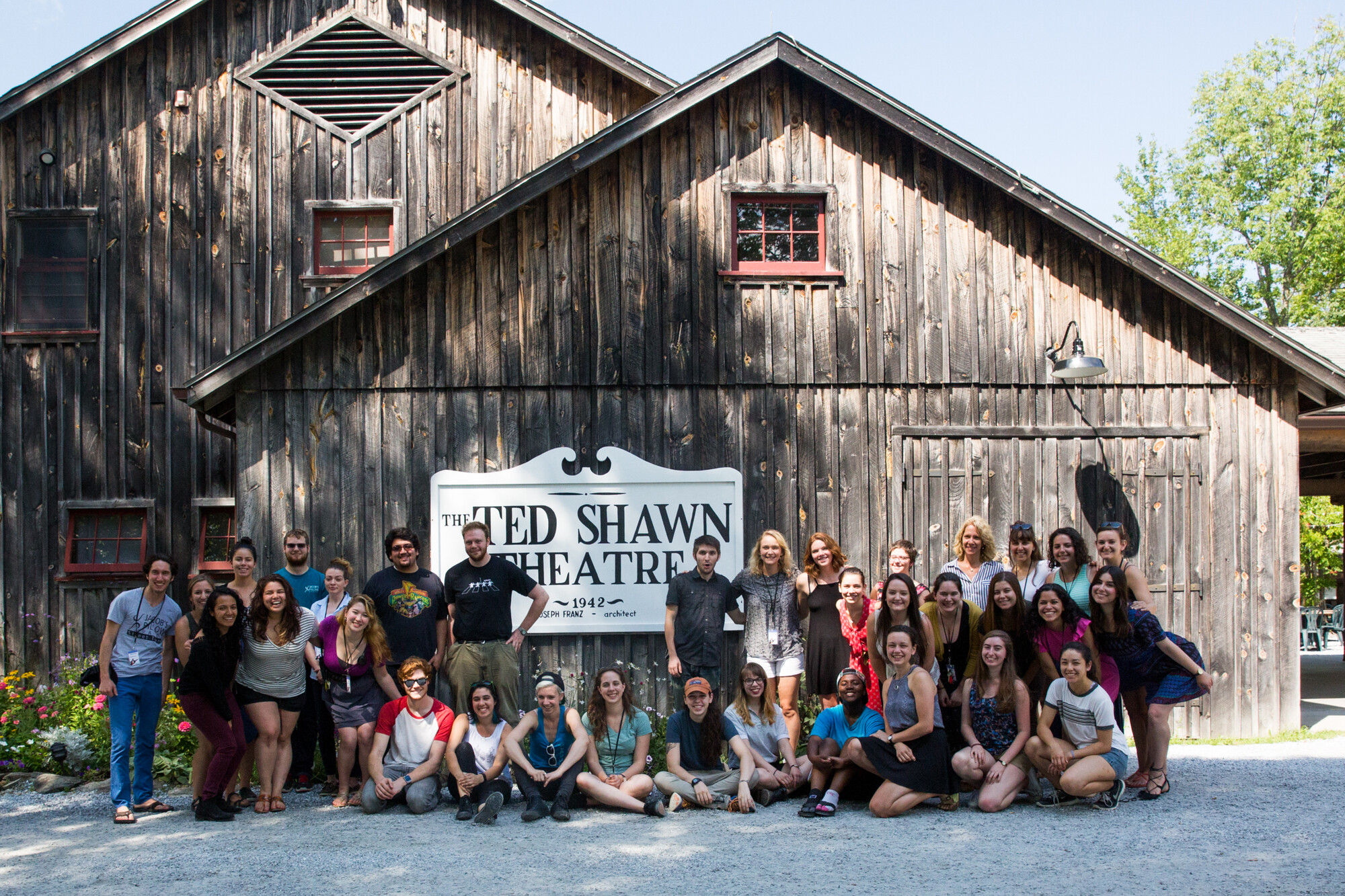 A large group of people standing in front of a small barn and smiling.