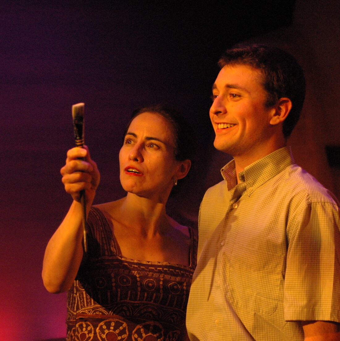 A woman holds a paintbrush and stares at it, along with a man standing next to her.