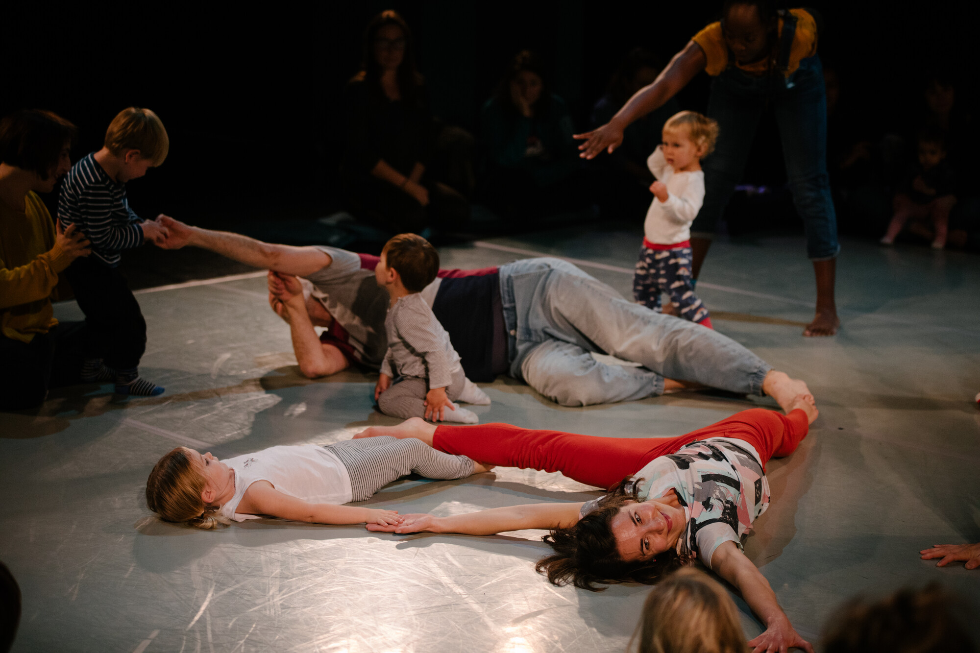 Five adults lay on stage and perform alongside three young children.