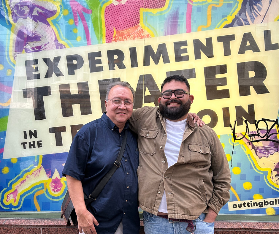 Two men posing for a picture in front of a wall that reads "Experimental Theater".