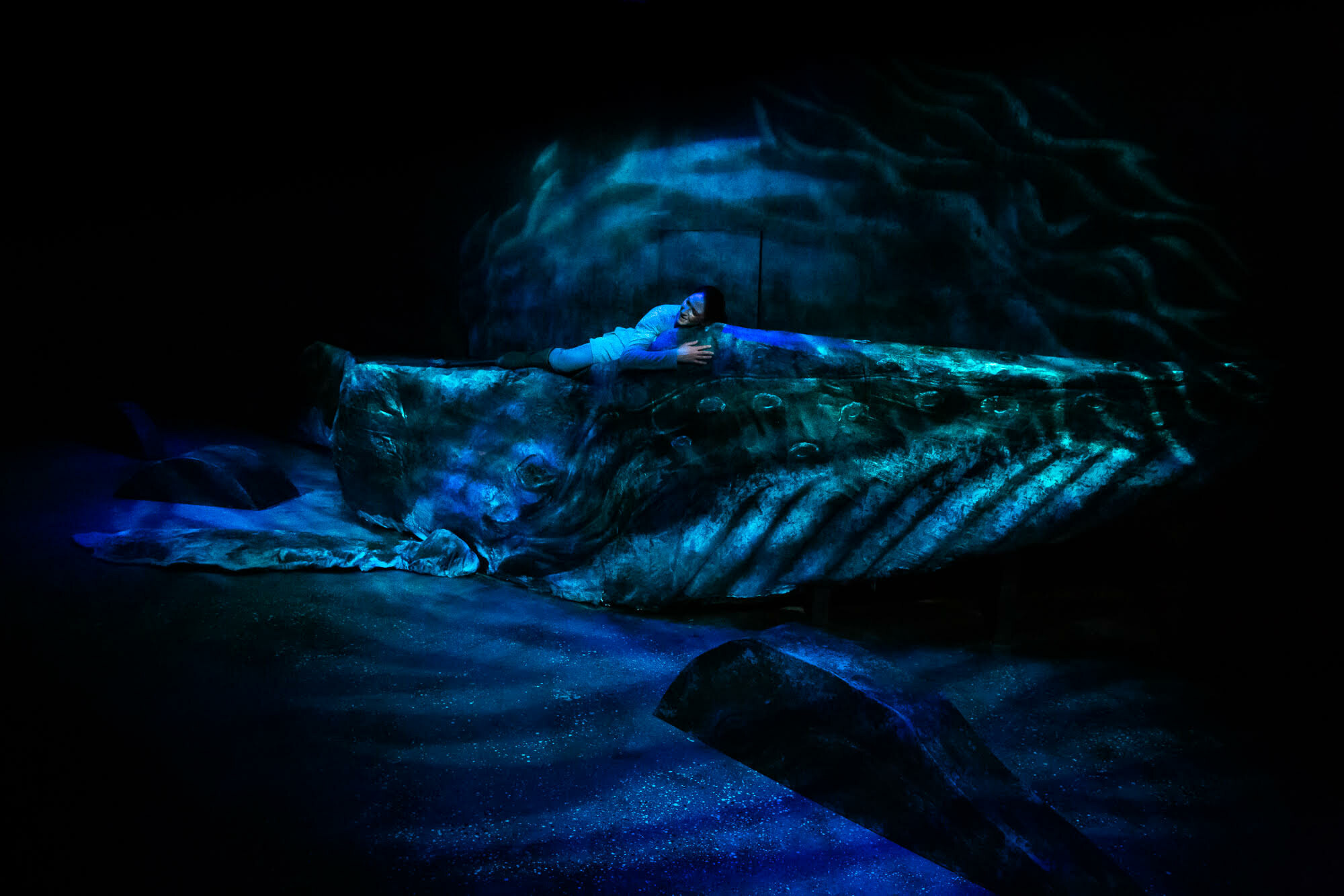 A performer lies down on a set piece that looks like a whale.