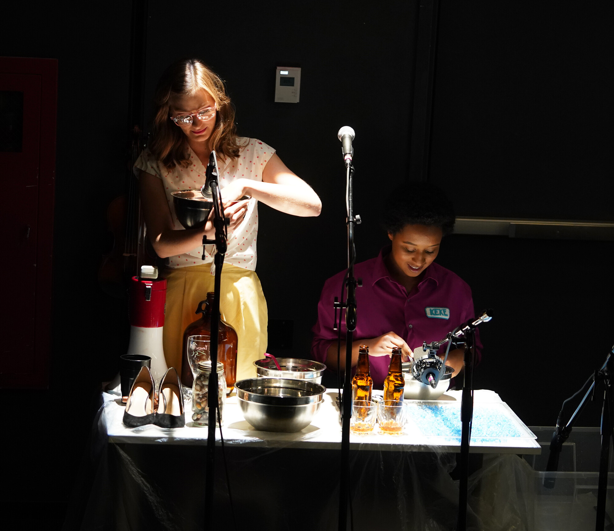 Two sound artists perform behind a table full of household objects.