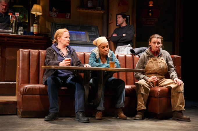 Three women sit in a restaurant booth on-stage.