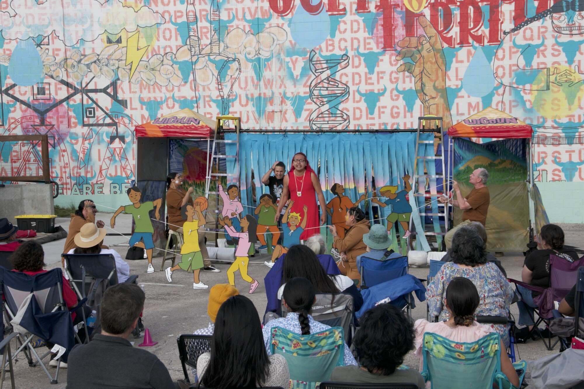 A performer speaks passionately while surrounded by puppets manipulated by other cast members.
