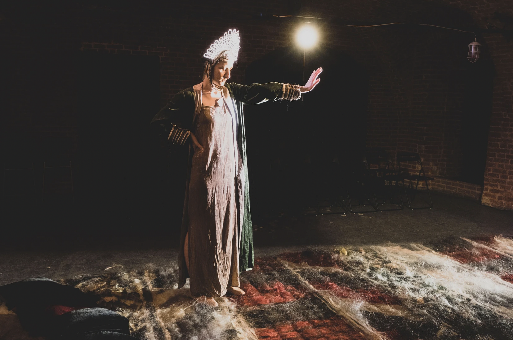 A woman wearing a lacey crown stands alone on a carpeted floor with a hand extended in a "halt" gesture.