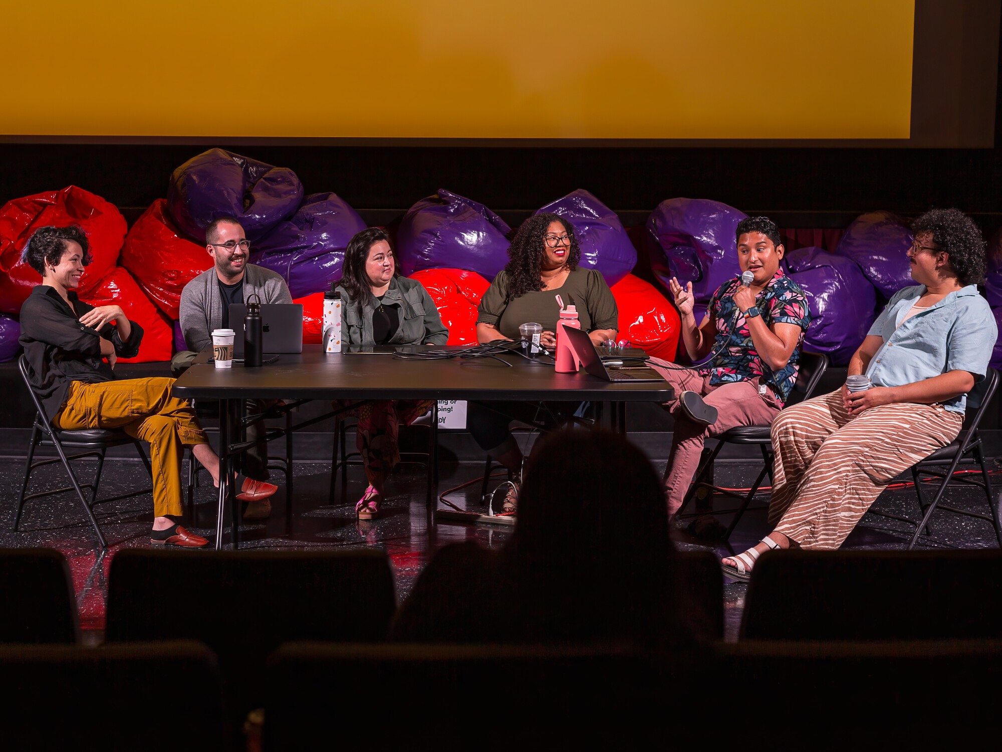 Six artists sit at a table on stage and speak during a panel.