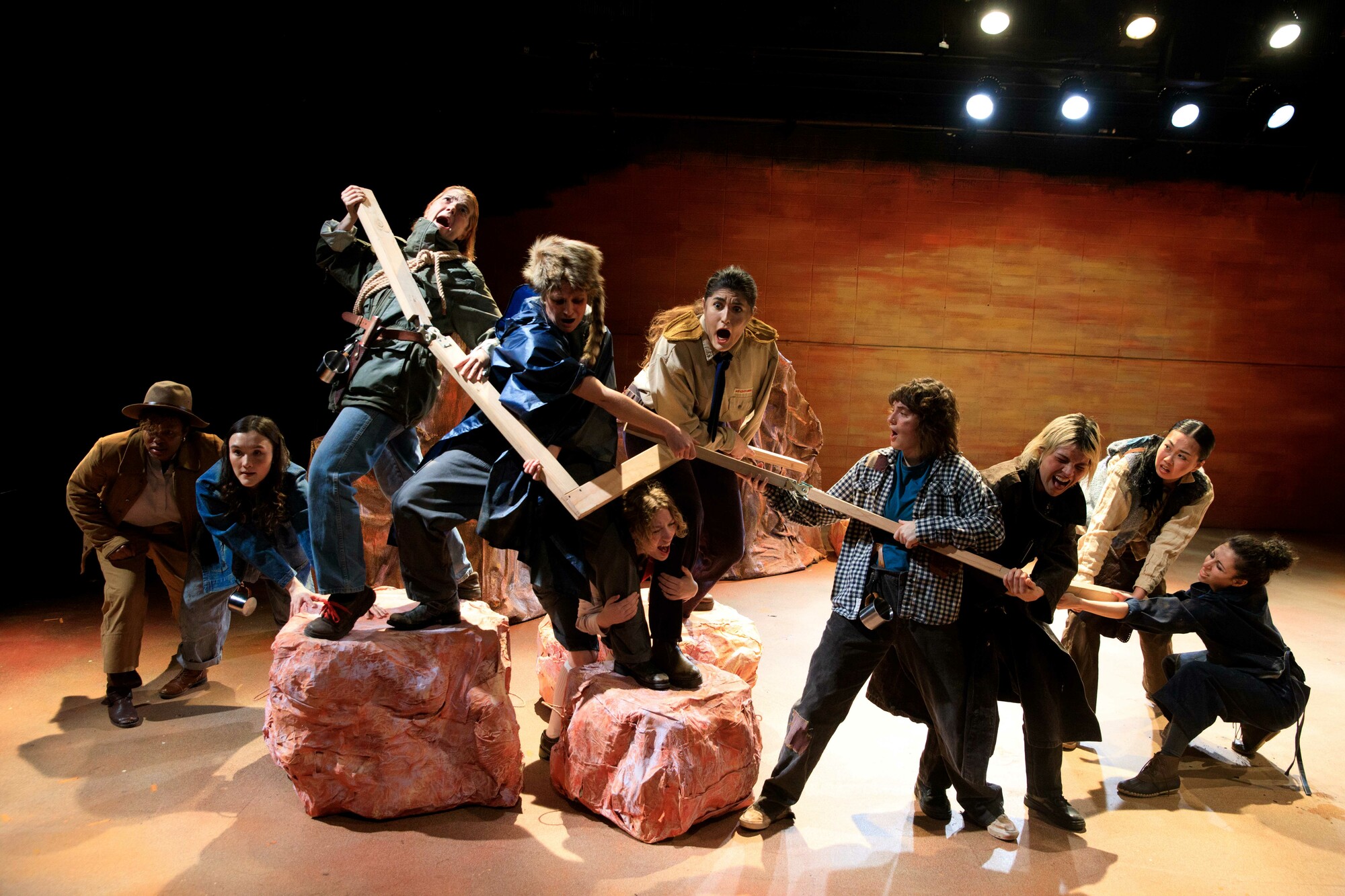 A group of actors onstage manipulate a large wooden prop.