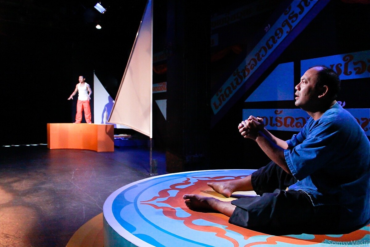 On the left, a performer stands on top of a curved platform and speaks. On the right, a performer sits on a round platform with hands clasped together.