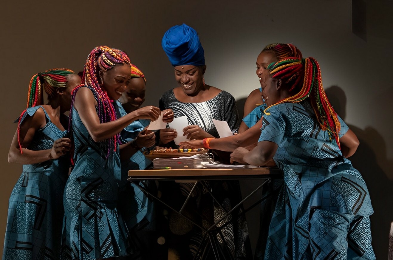 Six women gather around a table and smile while reading small letters.