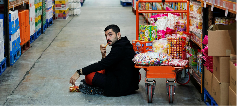 A man sitting on the floor of a warehouse and eating candy.
